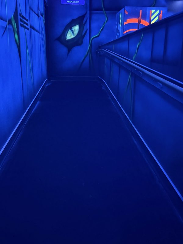 A painted reptile eye on the wall beside a dark ramp through the arena